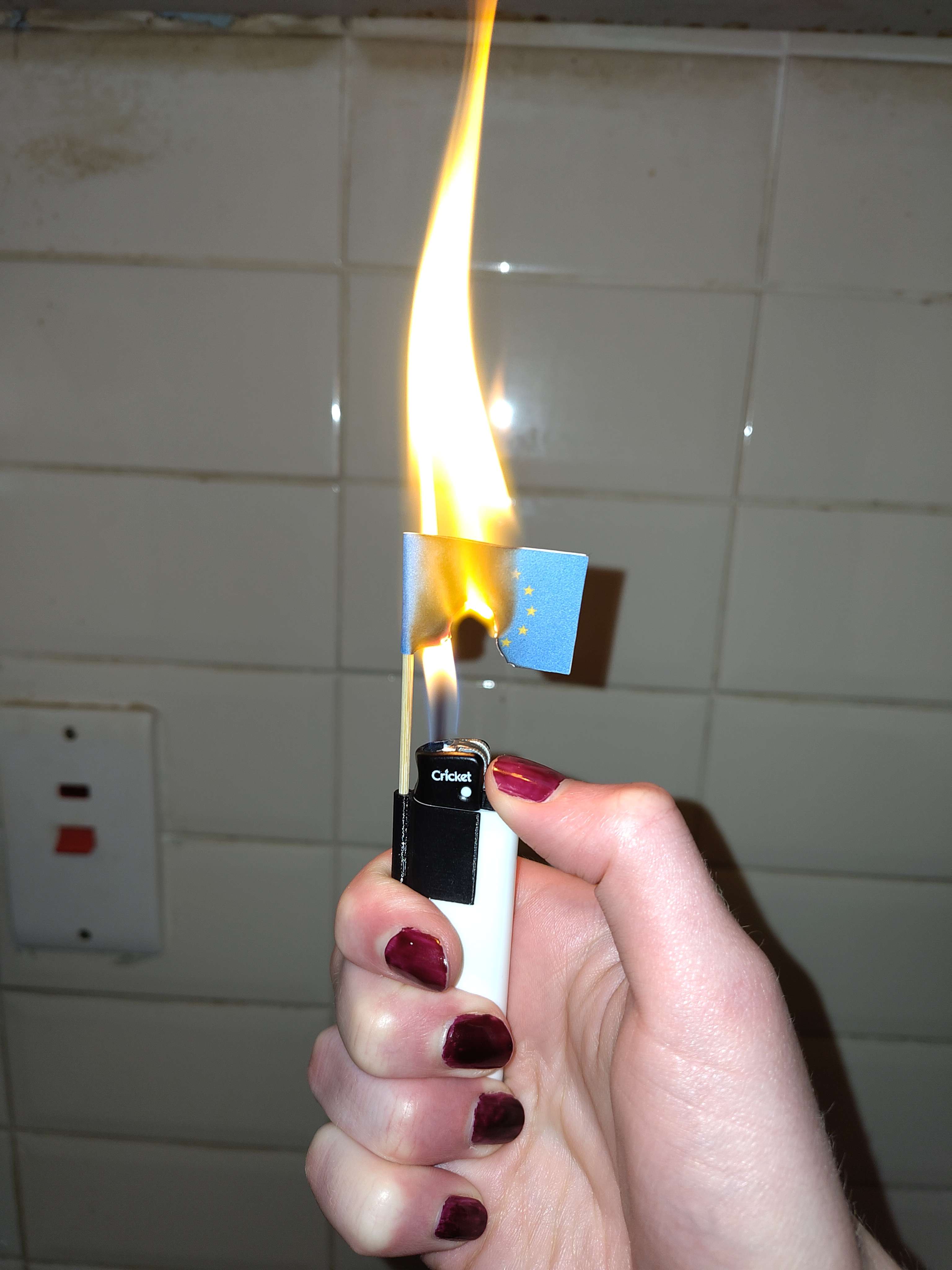 Lighter with a tiny EU flag attached to it. The flag is burning.